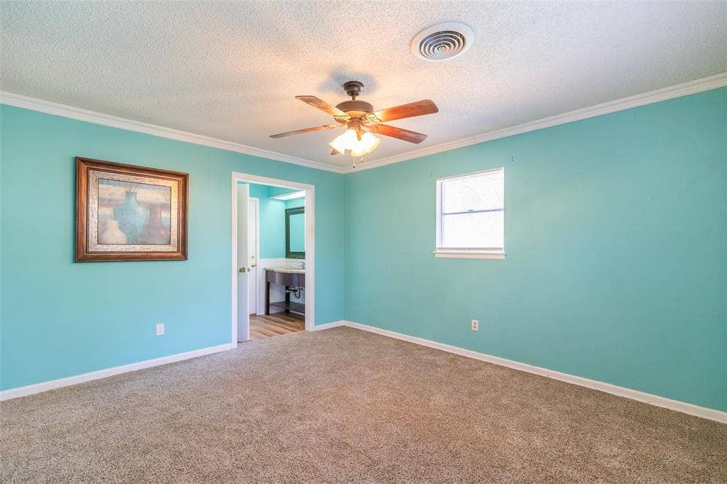 Carpeted flooring, ceiling fan with integrated lighting, single window, and a doorway opening to an additional space featuring wood-finish flooring and a vanity with an integrated sink