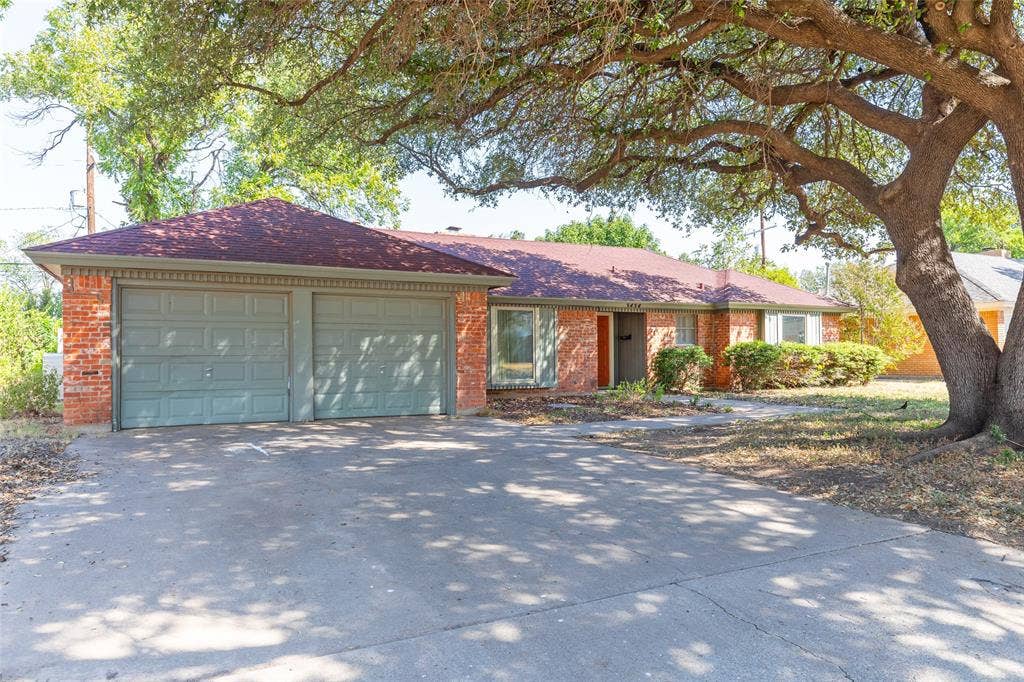 Brick exterior with a shingle roof, attached two-car garage, and mature tree