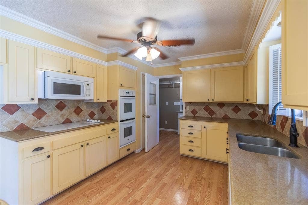 Kitchen featuring wood-finish flooring, cream cabinetry, a built-in microwave, double wall ovens, and a dual basin sink