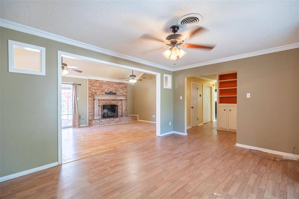 Wood-finish flooring throughout, ceiling fan with integrated lighting, built-in shelving, fireplace with brick surround, and white trim