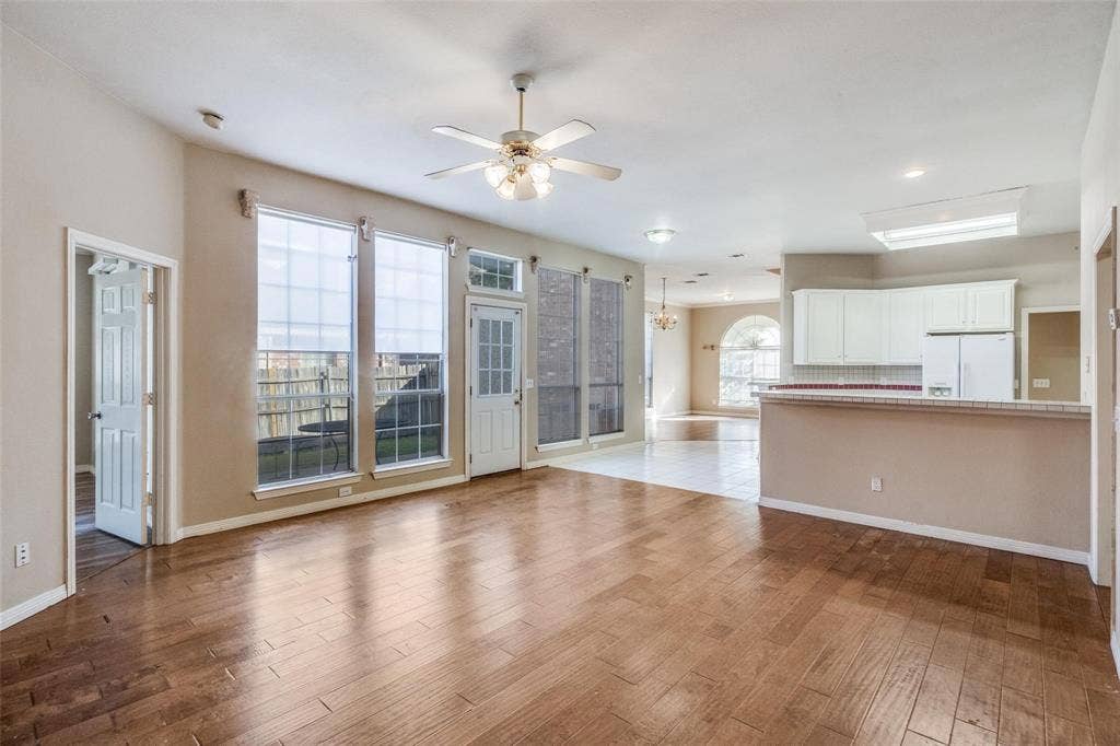 2305 Pittner Lane, Plano, TX 75025 Wood-finish flooring, ceiling fan with light fixture, multiple large windows with blinds, white kitchen cabinetry, and a kitchen island with a tiled backsplash
