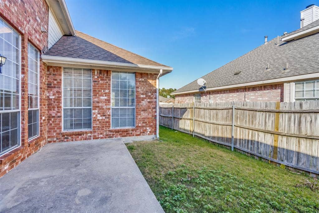 2305 Pittner Lane, Plano, TX 75025 Brick exterior with multiple windows, concrete patio, and sloped grass area