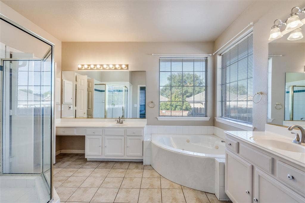 2305 Pittner Lane, Plano, TX 75025 Shower enclosure with clear glass, corner jetted tub, dual vanities with white cabinetry, large mirror, and tiled flooring