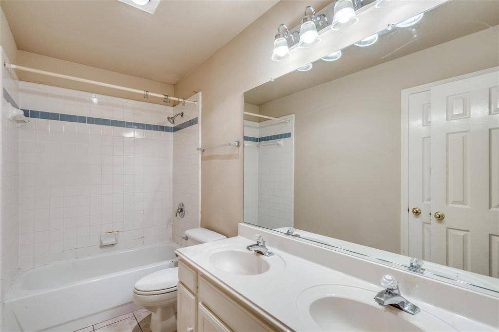 2305 Pittner Lane, Plano, TX 75025 Dual vanity with integrated sinks, full-width mirror, white paneled doors, and a tiled tub/shower combination