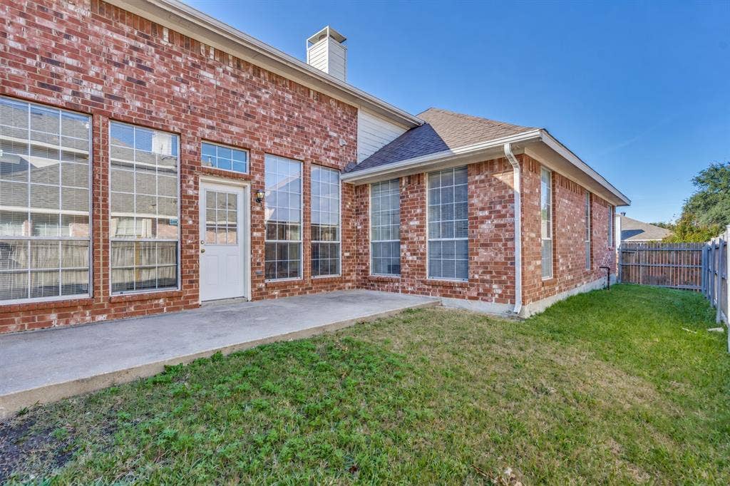 2305 Pittner Lane, Plano, TX 75025 Brick exterior with multiple tall windows, concrete patio, white rear entry door, and a grass lawn