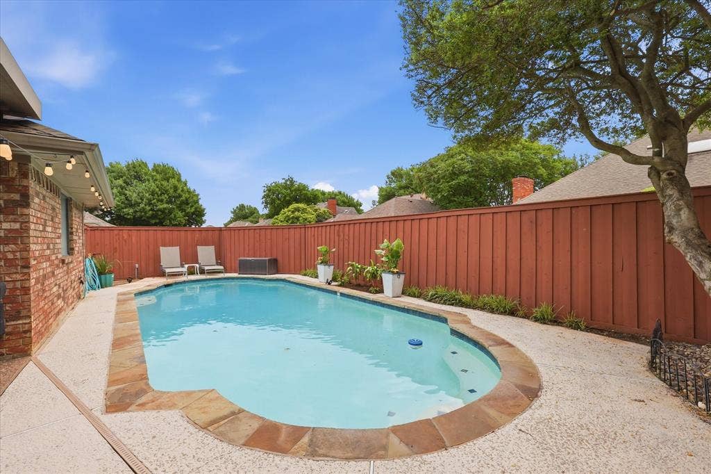 1516 Glastonbury Drive, Plano, TX 75075 Private backyard featuring a swimming pool with stone coping, textured concrete patio, and a high wood fence