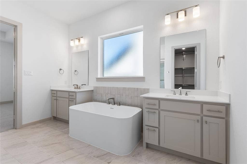 4524 Sunfish Lane, McKinney, TX 75071 Freestanding soaking tub with a tiled surround, dual vanities with integrated sinks, and neutral-toned tile flooring