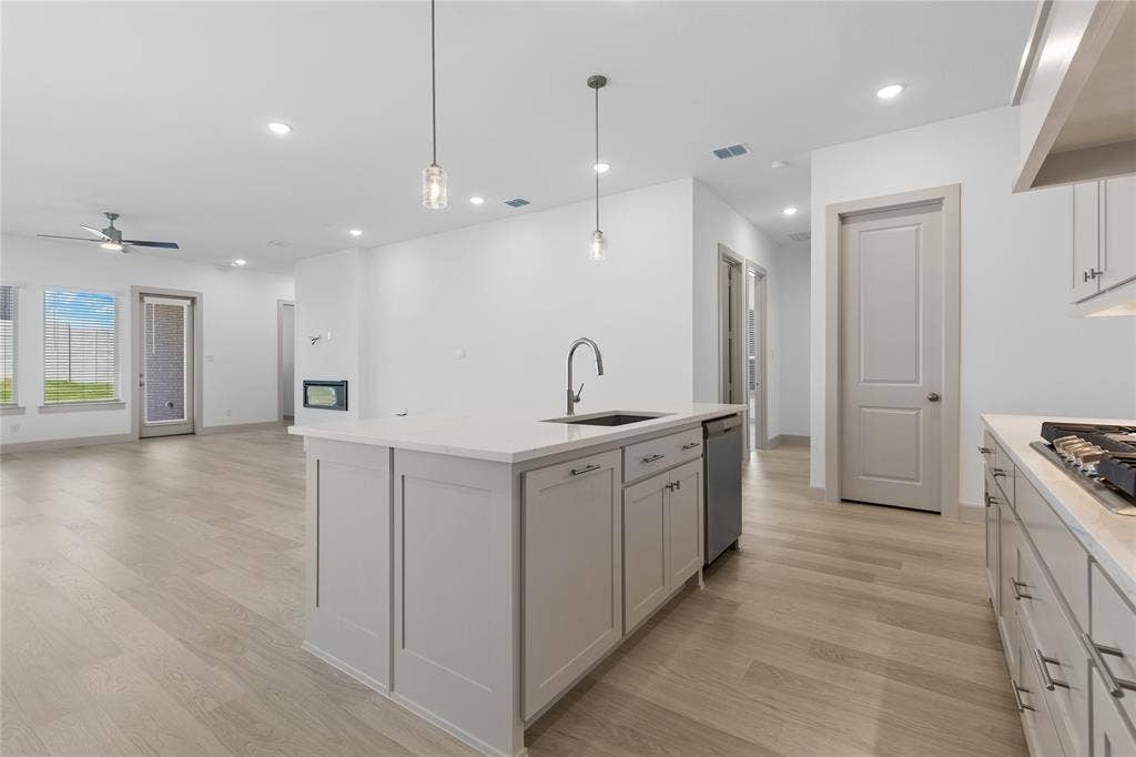 4524 Sunfish Lane, McKinney, TX 75071 Kitchen island with integrated sink, stainless steel dishwasher, light wood-finish flooring, recessed lighting, and modern pendant lights