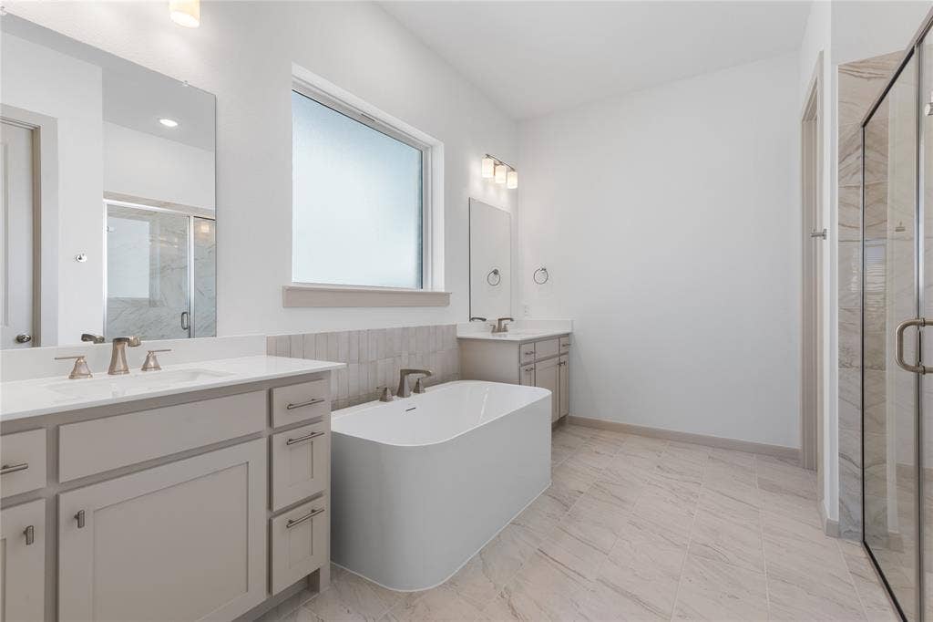 4524 Sunfish Lane, McKinney, TX 75071 Dual vanities with quartz countertops, a freestanding soaking tub, a large window, a glass-enclosed shower, and tile flooring
