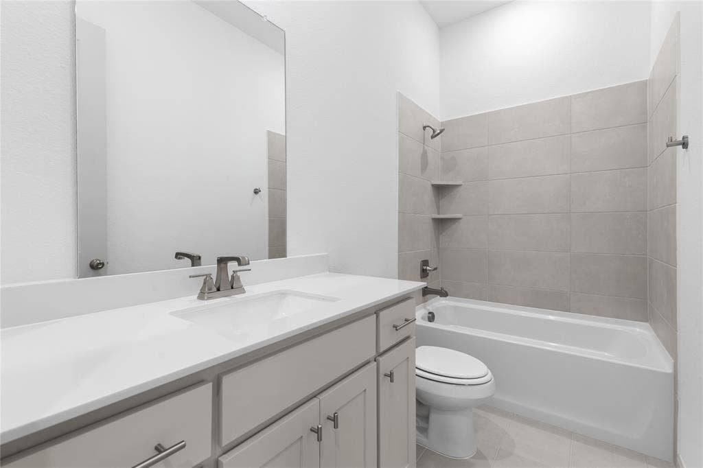4524 Sunfish Lane, McKinney, TX 75071 Modern bathroom featuring a single vanity with a white countertop and undermount sink, a large wall-mounted mirror, and a bathtub with tiled surround and built-in shelving