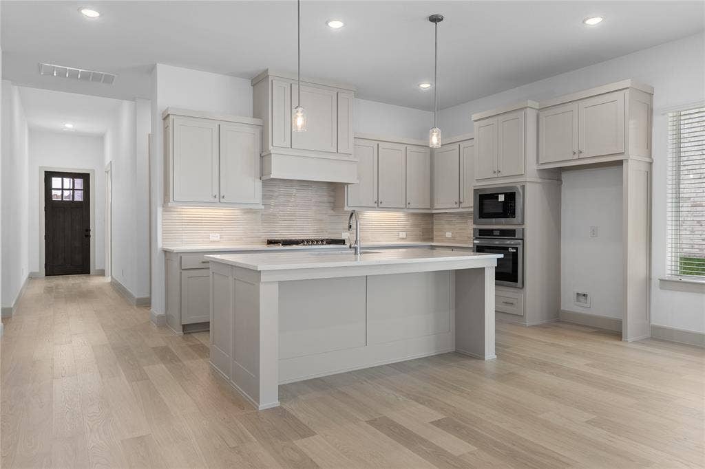4524 Sunfish Lane, McKinney, TX 75071 Gourmet kitchen with light-toned cabinetry, a spacious island, built-in stainless steel appliances, and wood-finish flooring