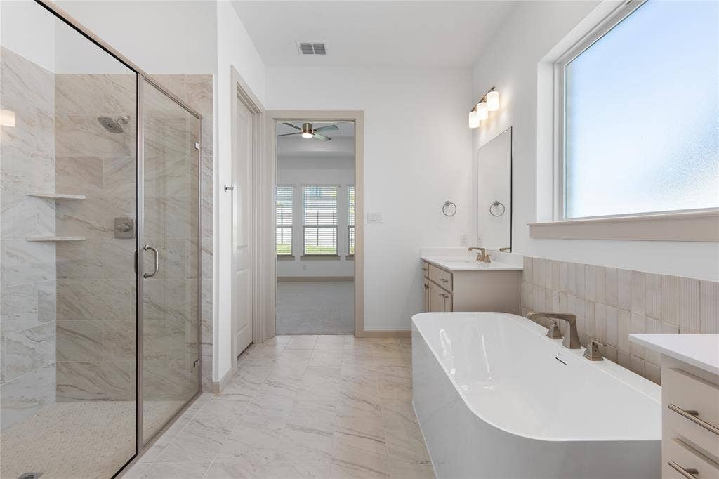 4524 Sunfish Lane, McKinney, TX 75071 Contemporary bathroom featuring a freestanding soaking tub, glass-enclosed shower with built-in shelving, dual vanity with undermount sinks, and large format tile flooring