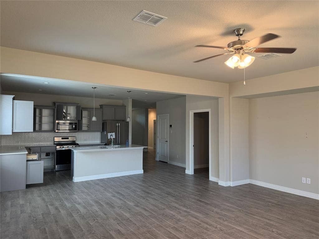 5213 Meadow Lane, Krum, TX 76249 Open-concept living area featuring wood-finish flooring, a ceiling fan with integrated lighting, and a kitchen with stainless steel appliances, grey cabinetry, and an island with a sink