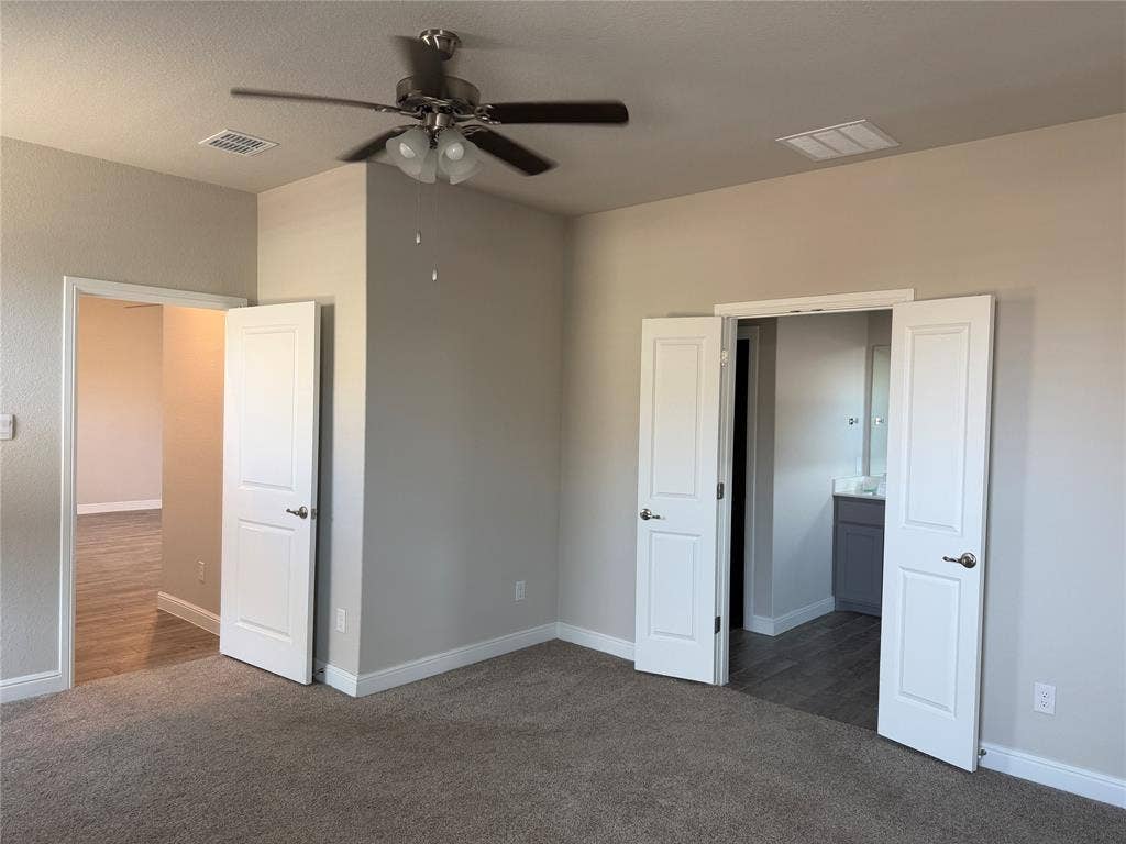 5213 Meadow Lane, Krum, TX 76249 Carpeted flooring, neutral wall tones, ceiling fan with integrated lighting, white paneled doors, and wood-look flooring visible through doorways