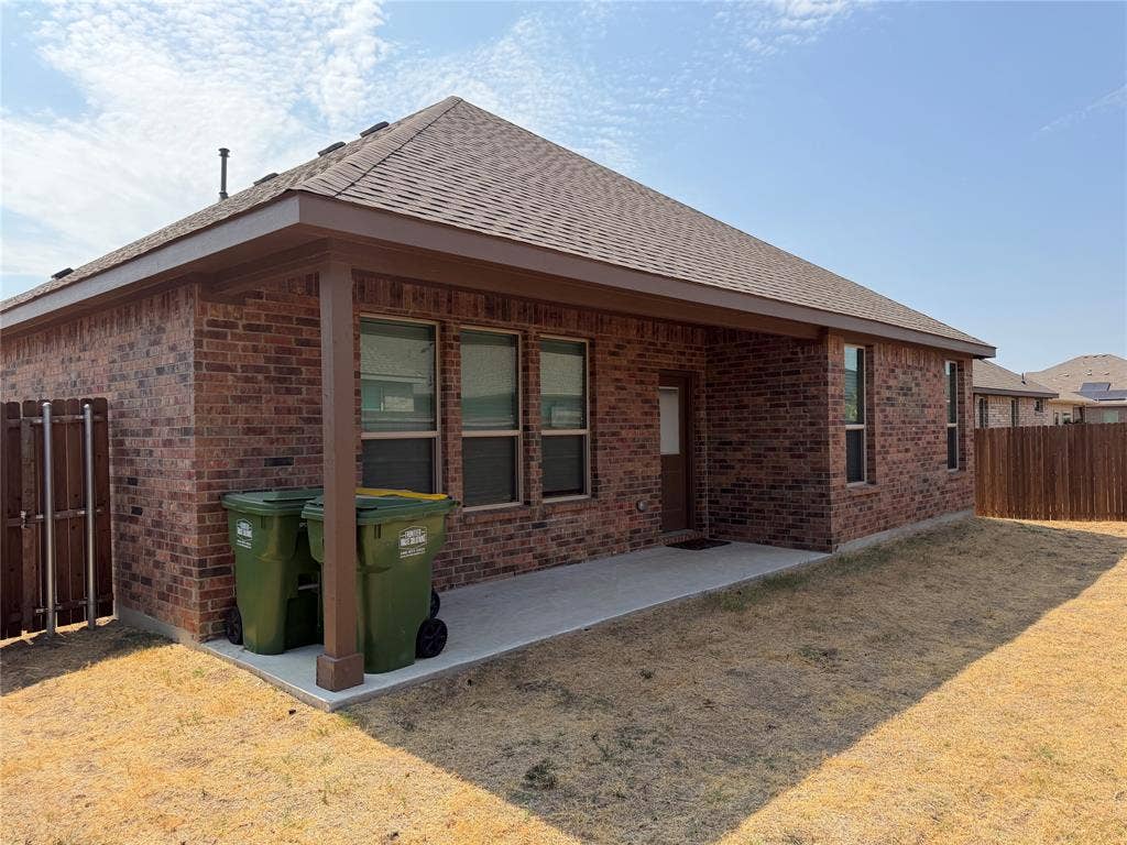 5213 Meadow Lane, Krum, TX 76249 Brick exterior with a covered patio, concrete slab, and wood privacy fencing
