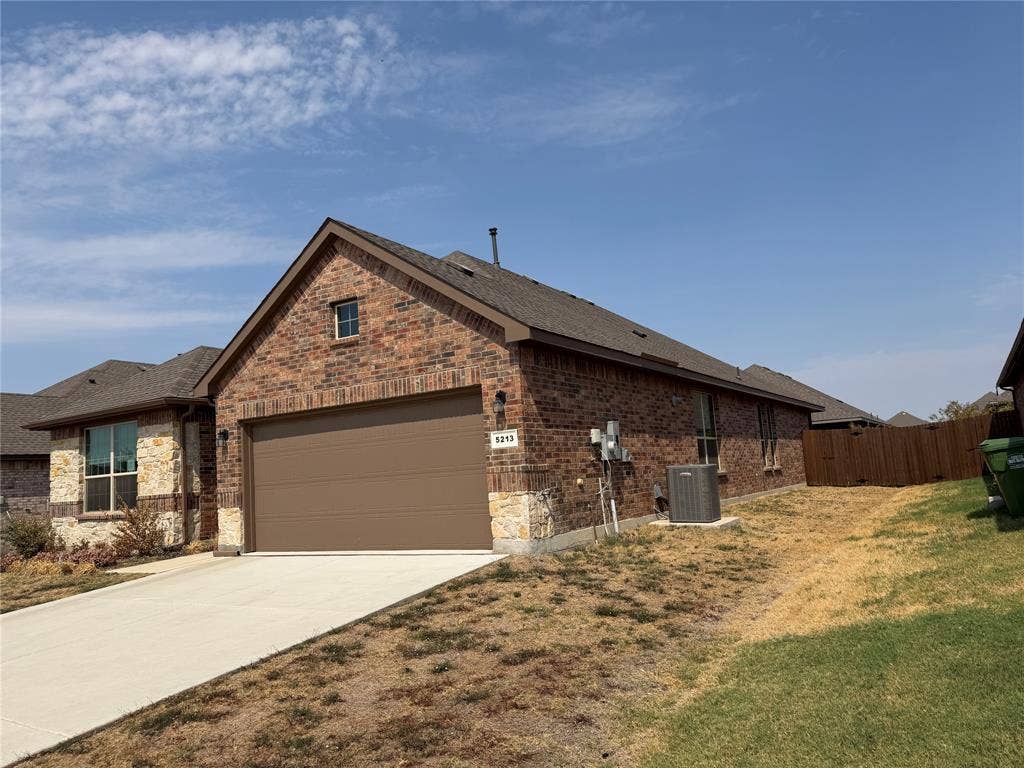 5213 Meadow Lane, Krum, TX 76249 Brick and stone exterior with a brown garage door, concrete driveway, and gabled roofline