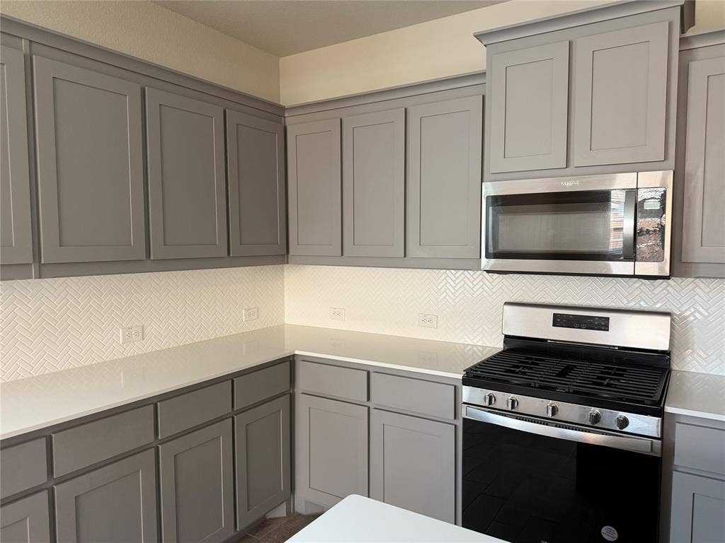 5213 Meadow Lane, Krum, TX 76249 Neutral-toned cabinetry, white herringbone tile backsplash, stainless steel microwave, gas range, and light-colored countertops