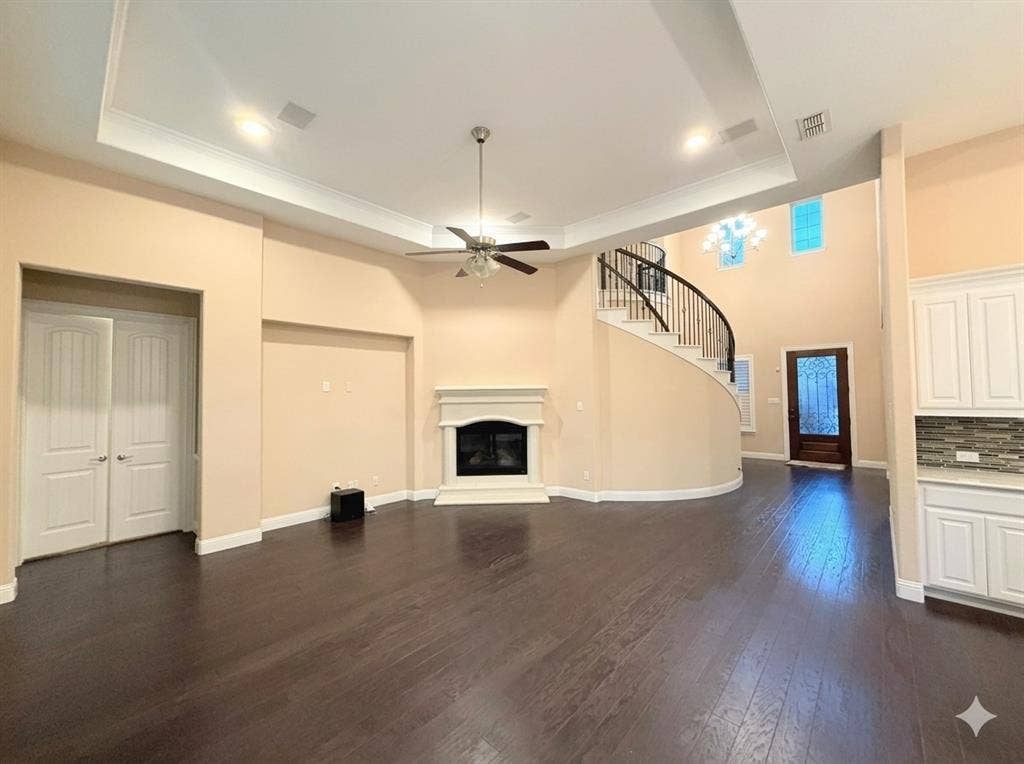 5917 Trantina Lane, Frisco, TX 75035 Dark wood-finish flooring, a curved staircase with wrought iron balusters, a fireplace with a white mantel, white cabinetry with a tile backsplash, and a tray ceiling