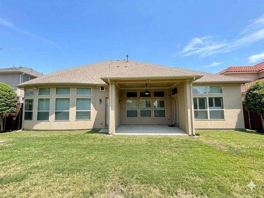 5917 Trantina Lane, Frisco, TX 75035 Expansive backyard featuring a covered patio, multiple large windows, stucco exterior, and a shingle roof