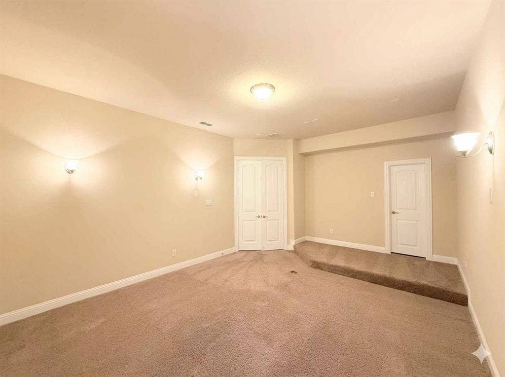 5917 Trantina Lane, Frisco, TX 75035 Carpeted room with a raised platform, two wall sconces, a ceiling-mounted light fixture, and two white panel doors