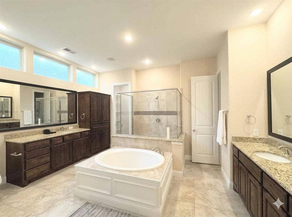 5917 Trantina Lane, Frisco, TX 75035 Large bathroom featuring a built-in soaking tub, a separate glass-enclosed shower, dual vanities with granite countertops, and extensive dark wood-finish cabinetry