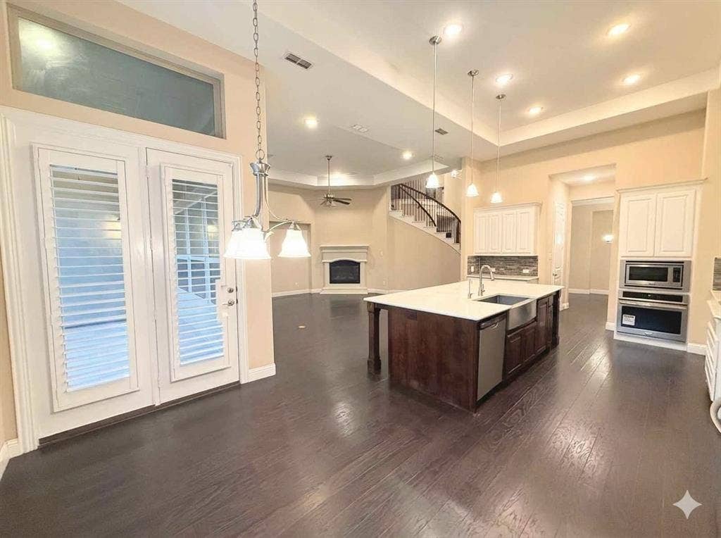 5917 Trantina Lane, Frisco, TX 75035 Spacious open-concept interior featuring wood-finish flooring, a kitchen island with a farmhouse sink, integrated stainless steel appliances, and a curved staircase