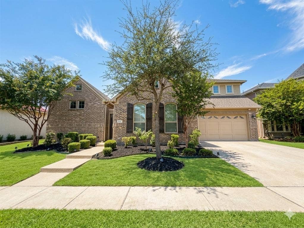 5917 Trantina Lane, Frisco, TX 75035 Brick exterior, arched windows with shutters, attached two-car garage, concrete driveway, and established landscaping