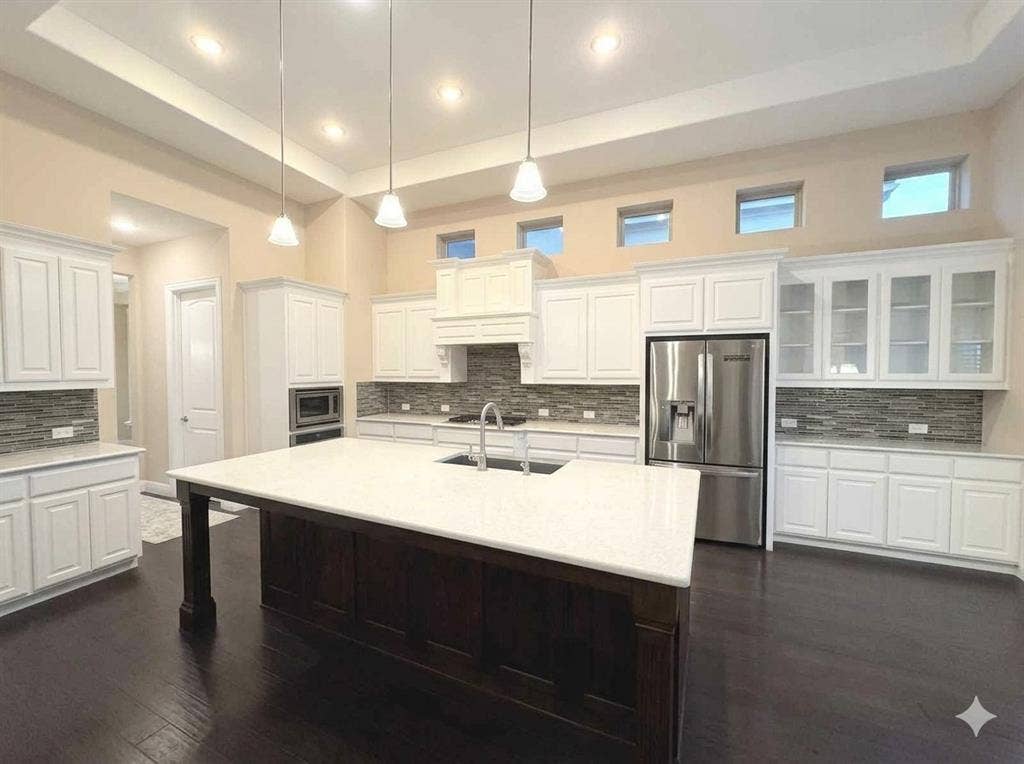 5917 Trantina Lane, Frisco, TX 75035 Kitchen featuring a large central island with a light-toned countertop, white cabinetry with glass-front uppers, stainless steel appliances, and dark wood-finish flooring