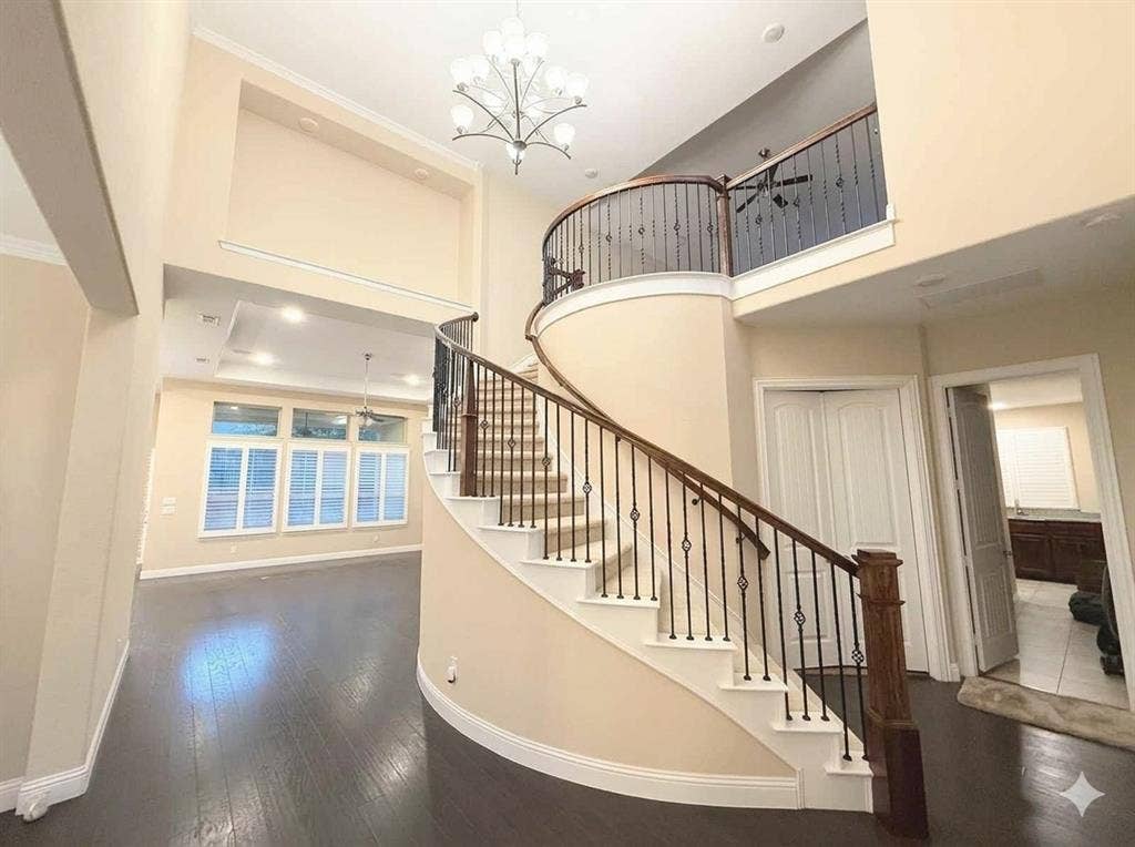 5917 Trantina Lane, Frisco, TX 75035 Curved staircase with decorative wrought iron spindles, wood-finish flooring, and high ceilings with an ornate chandelier