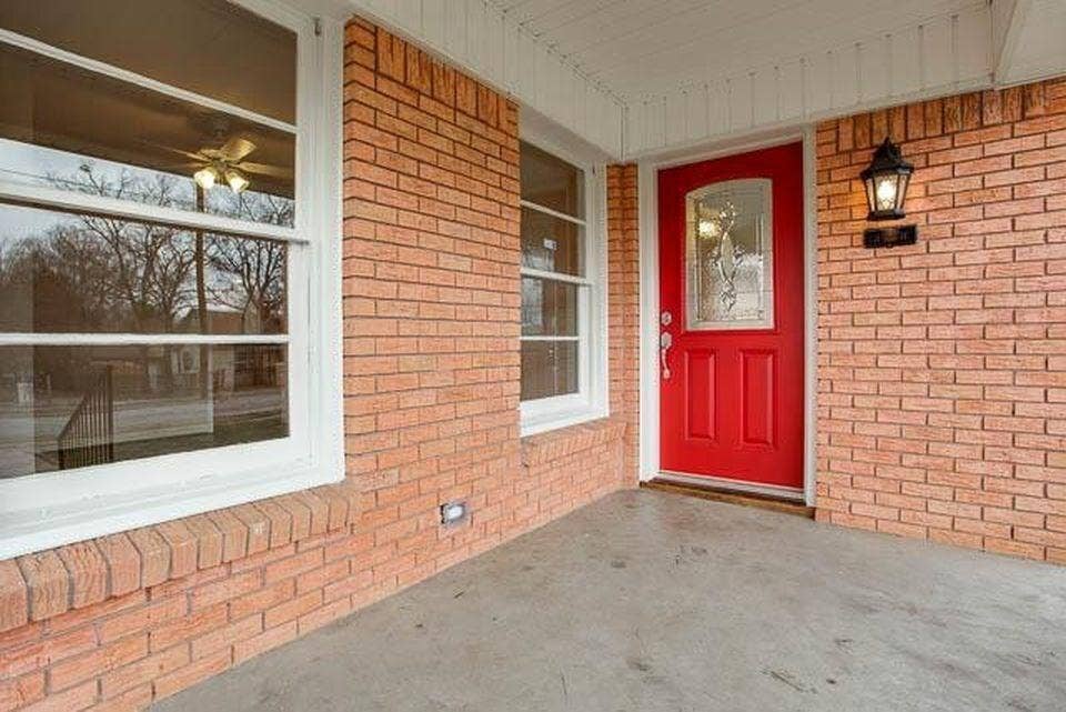 Brick exterior with a vibrant red front door, decorative glass insert, and a wall-mounted lantern light fixture