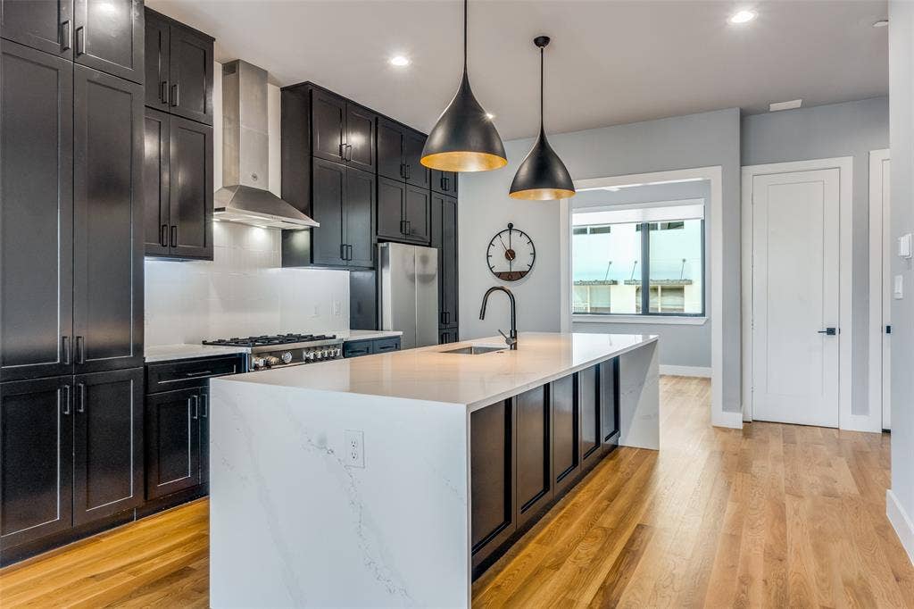 805 Pavillion Street, #103, Dallas, TX 75204 Open-concept kitchen featuring dark cabinetry, a gas range with stainless steel hood, a large island with a waterfall countertop, and wood-finish flooring