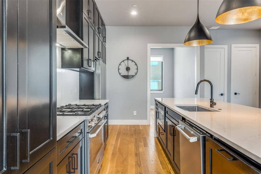 805 Pavillion Street, #103, Dallas, TX 75204 Kitchen featuring dark cabinetry, stainless steel appliances, a center island with sink, pendant lighting, and wood-finish flooring