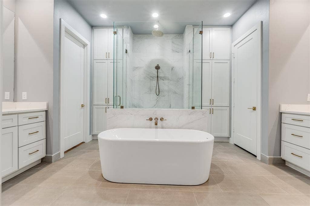 805 Pavillion Street, #103, Dallas, TX 75204 Freestanding soaking tub, dual vanities with stone countertops, glass-enclosed shower, built-in cabinetry, and tile flooring