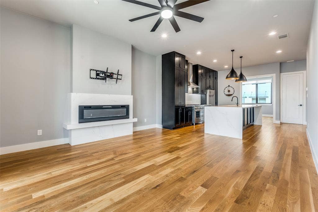 805 Pavillion Street, #103, Dallas, TX 75204 Engineered wood flooring, modern electric fireplace, recessed lighting, black shaker-style cabinetry, and a waterfall island with a sink
