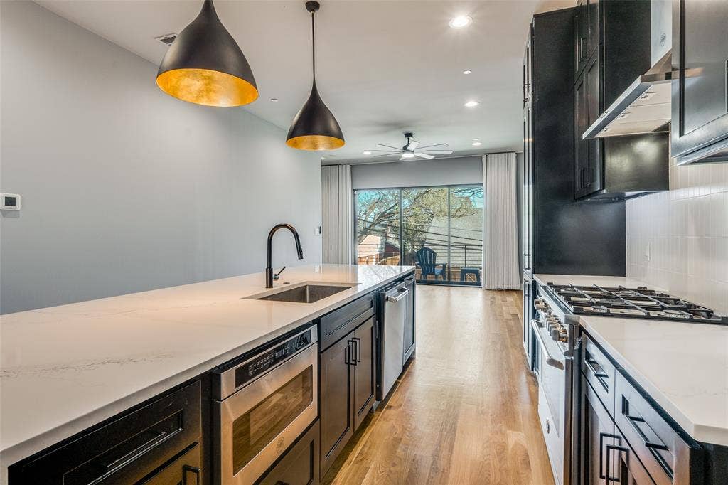 805 Pavillion Street, #103, Dallas, TX 75204 Contemporary kitchen featuring a built-in microwave, stainless steel appliances, wood-finish flooring, and pendant lighting