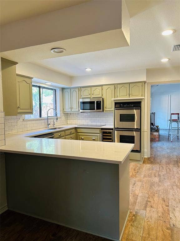 3713 San Juan Circle, Plano, TX 75023 U-shaped kitchen with light green cabinetry, white subway tile backsplash, stainless steel appliances, and wood-finish flooring