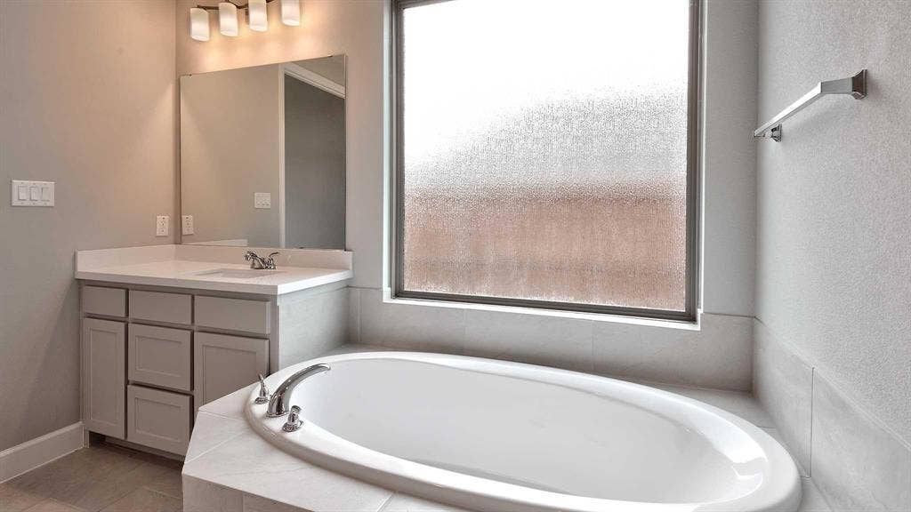 4237 Capstone Road, Midlothian, TX 76065 Built-in bathtub with deck-mounted fixtures, vanity with undermount sink, countertop, mirror, and wall-mounted light fixture
