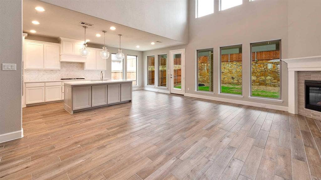 4237 Capstone Road, Midlothian, TX 76065 Open-concept living space featuring wood-finish flooring, a contemporary kitchen island with pendant lighting, a tile-surround fireplace, and expansive windows