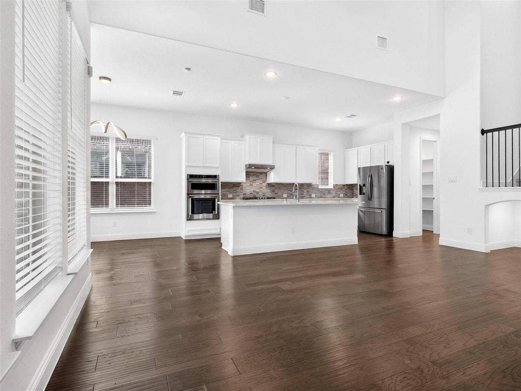 6504 Dynamite Drive, McKinney, TX 75070 Open-concept living space featuring high ceilings, dark wood-finish flooring, and a kitchen with white cabinetry, stainless steel appliances, and a tiled backsplash