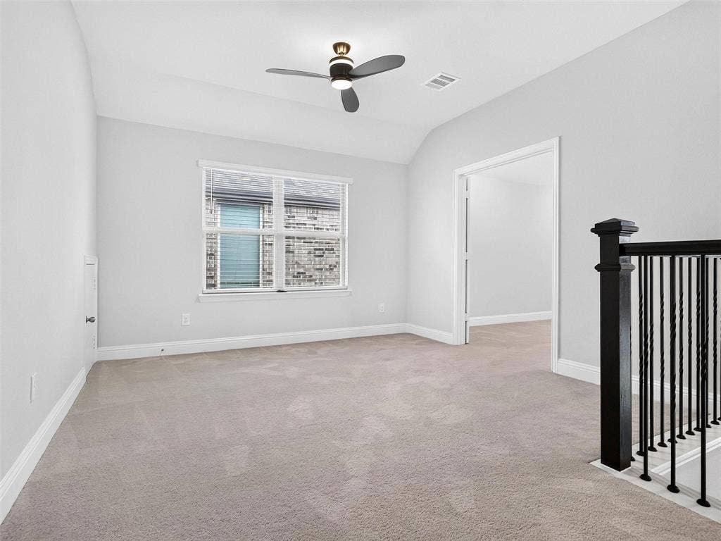 6504 Dynamite Drive, McKinney, TX 75070 Neutral-toned carpeting, ample natural light from a large window, a ceiling fan, and a black wrought iron newel post and baluster