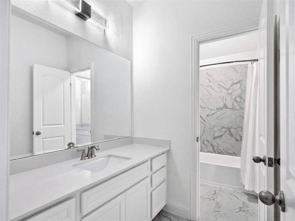 6504 Dynamite Drive, McKinney, TX 75070 White vanity with a built-in sink and brushed nickel faucet, large wall mirror, and modern vanity lighting