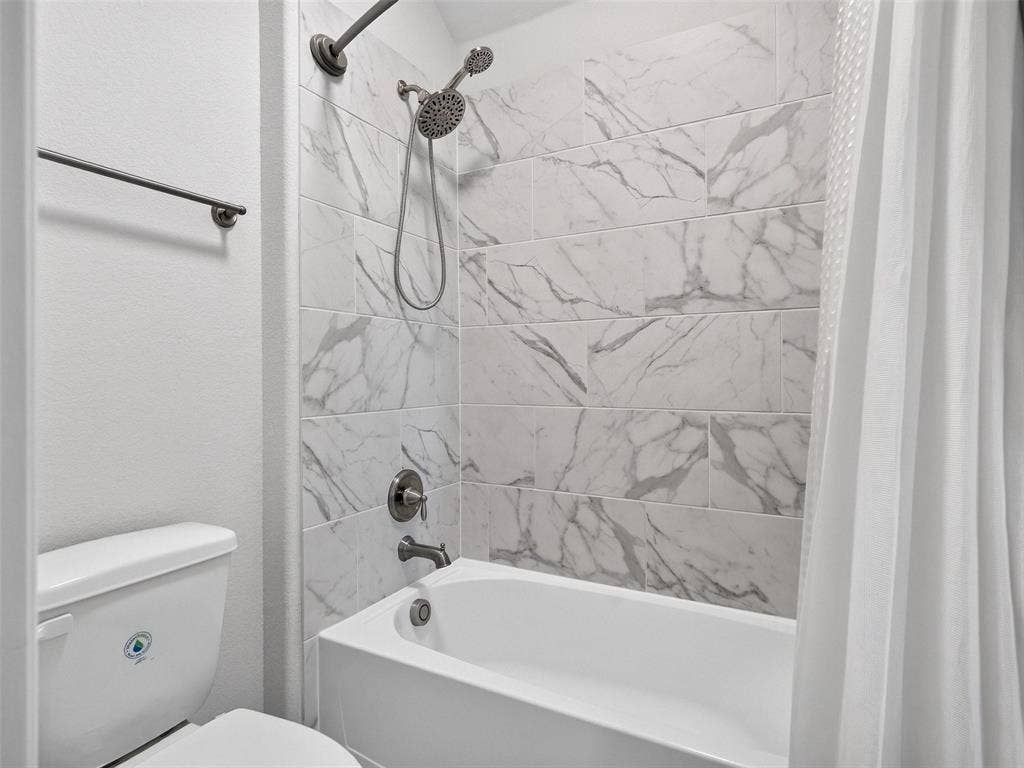 6504 Dynamite Drive, McKinney, TX 75070 Bathtub and shower combination featuring a tiled surround with a marble-look finish and a brushed nickel shower fixture