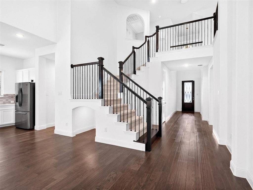 6504 Dynamite Drive, McKinney, TX 75070 Expansive open concept interior featuring wood-finish flooring, a grand staircase with wrought iron balusters, a second-story landing, and a vaulted ceiling