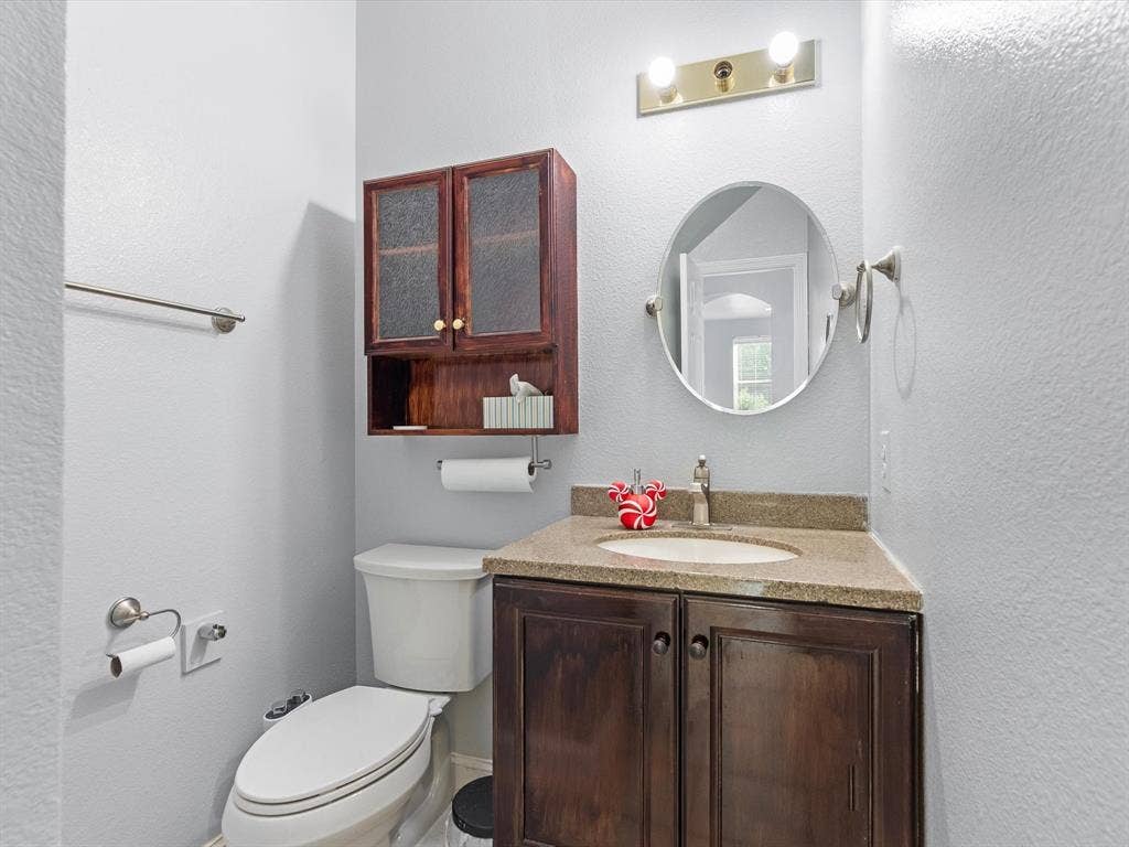 7302 San Carlos Drive, Rowlett, TX 75089 Vanity with a granite-style countertop, undermount sink, dark wood-finish cabinetry, and an oval mirror