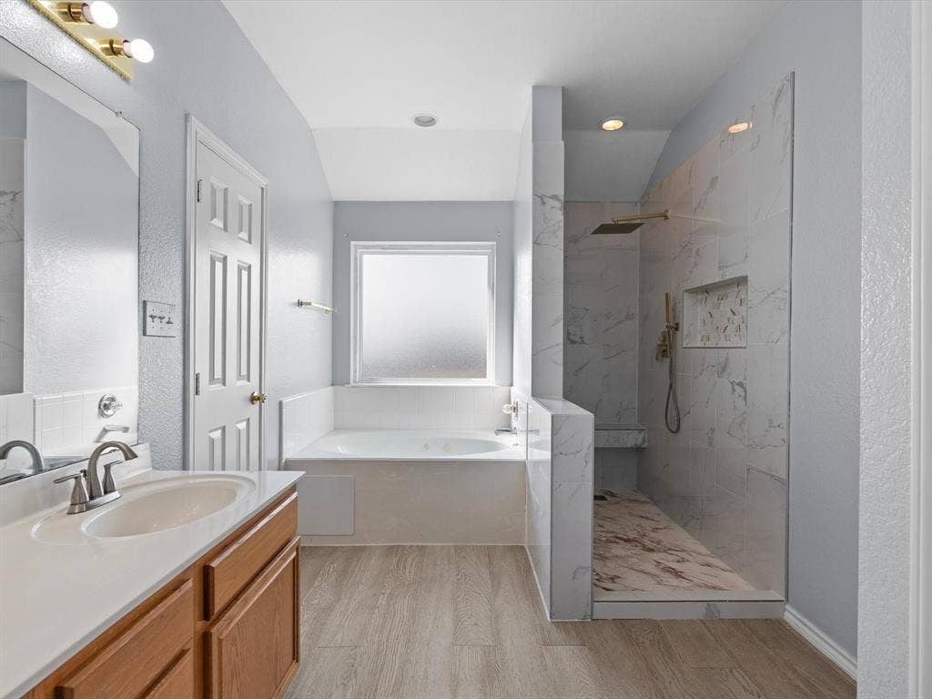 7302 San Carlos Drive, Rowlett, TX 75089 Walk-in shower with a built-in bench and recessed shelf, freestanding tub, single vanity with a solid surface countertop, and wood-finish flooring