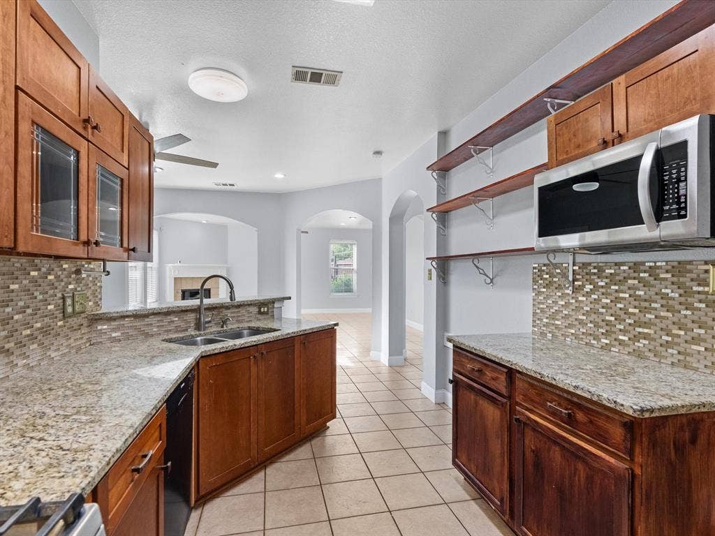 7302 San Carlos Drive, Rowlett, TX 75089 Kitchen featuring wood cabinetry, granite countertops, a stainless steel microwave, tile flooring, and a mosaic tile backsplash