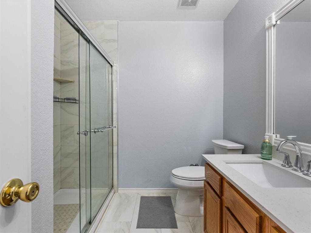 7302 San Carlos Drive, Rowlett, TX 75089 Glass-enclosed shower with tiled surround, wood-finish vanity with countertop, undermount sink, and polished chrome fixtures
