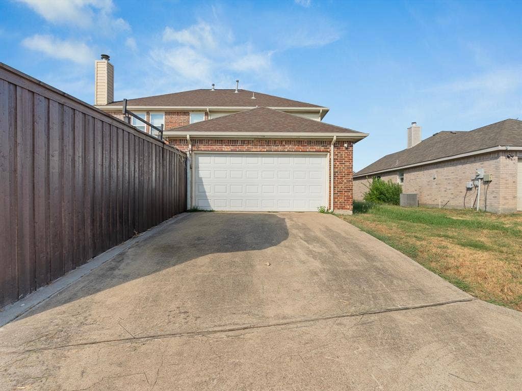 7302 San Carlos Drive, Rowlett, TX 75089 Brick facade with an attached garage, featuring a concrete driveway and privacy fencing