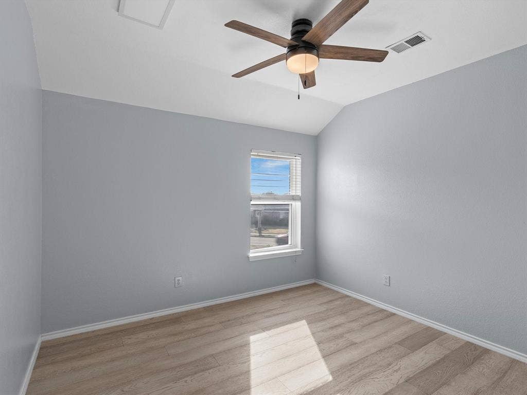 7302 San Carlos Drive, Rowlett, TX 75089 Wood-finish flooring, light blue walls, single window with blinds, vaulted ceiling, and a ceiling fan with integrated lighting