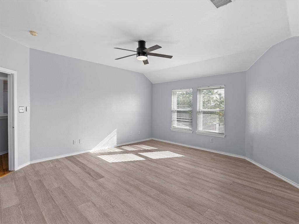 7302 San Carlos Drive, Rowlett, TX 75089 Wood-finish flooring, light blue wall paint, two windows with blinds, and a ceiling fan with integrated lighting